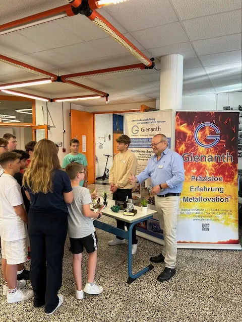 Ausbilder am Messestand von Gienanth erklärt Jugendlichen ein Werkstück